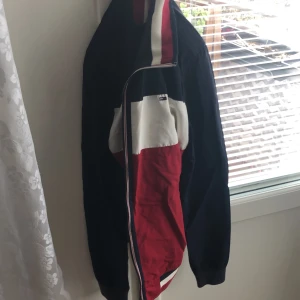 Flerfärgad jacka från Tommy Jeans - Säljer en snygg flerfärgad jacka från Tommy Jeans. Jackan har en dragkedja och är i färgerna blå, röd och vit. Perfekt för en sportig look!
