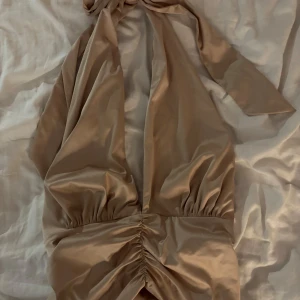 Beige topp från Gina Tricot - Snygg beige halternecktopp från Gina Tricot med knytning i nacken och rynkade detaljer i midjan. Aldrig använd! Perfekt till fest och sommarn, Storlek M🩷hör av dig vid intresse!