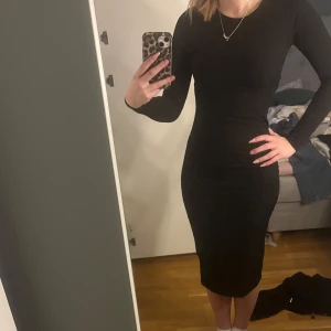 Svart långärmad klänning med öppen rygg - Snygg svart långärmad klänning med en elegant öppen rygg. Perfekt för en stilren look. Klänningen har en tight passform som framhäver figuren.