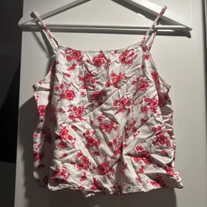 Vit blommig linnetopp - Söt vit linnetopp med röda/rosa blommor och smala axelband. Perfekt för sommardagar. Storlek S men liten i storleken så skulle säga att den är mer XS. 