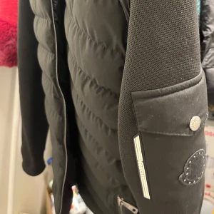 Diskret Svart jacka från Moncler - Snygg svart cardigain från Moncler med dragkedja och quiltad design.  Qr Koden fungerar i jackan. Storlek S. Moncler märket är diskret perfekt för dig som vill ha märkeskläder men inte skrikiga
