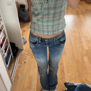 Rutig linnetopp från H&M, stl 36 - Supersöt rutig linnetopp från H&M i storlek 36. Toppen har tunna axelband, smockad struktur och knytning framtill. Färgerna är ljusblått/-grönt och beige. Passformen är croppad och toppen är luftig och lätt, men lite mindre i storleken. Den är väl använd då min mamma köpte den under 90-talet eller tidigt 00-tal.