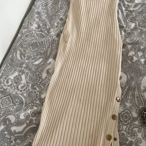 Beige ribbad klänning från NLY Trend - Säljer en beige ribbad klänning från NLY Trend i storlek XXS. Klänningen är ärmlös och har snygga metallknappar längs sidan. Den är figurnära och har en stilren, enkel design som känns modern och fräsch.