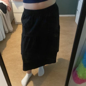 Svart långkjol med resårmidja - En svart långkjol med resår i midjan och lätt volang. Kjolen har en luftig och flowy passform, perfekt för dig som gillar en enkel men snygg stil. Materialet känns mjukt och bekvämt mot huden.