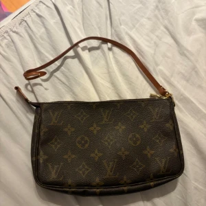 Louis Vuitton Monogram axelväska - Säljer en klassisk Louis Vuitton axelväska i brunt skinn med ikoniskt monogrammönster och guldfärgad dragkedja. Väskan har en smal, justerbar axelrem i ljust läder och rymligt fack. Perfekt för dig som gillar lyxiga accessoarer med tidlös design. Sönder vid en delar där man fäster bandet men går att laga ifall man skulle vilja de eller använda den utan bandet. Nypris 6000kr på merch Sweden, mitt pris 4000