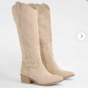Beige  boots - Säljer ett par snygga beige boots i mocka med spetsig tå och låg klack. Bootsens höga skaft har dekorativa sömmar som ger en cool western-vibe. Perfekt för dig som vill sticka ut med en trendig look.