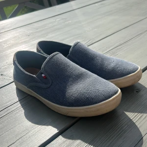 Tommy hilfiger slip-on sneakers  - Snygga slip-on sneakers från Tommy hilfiger i blått tyg, dom är i bra skick och väldigt sköna att gå i. Storlek 39