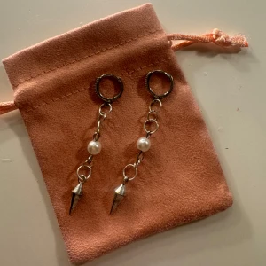 Silvriga örhängen med pärlor och spikes - Säljer ett par coola örhängen i silverfärg med kedjor, vita pärlor och spetsiga spikes längst ner. De har en modern vibe och passar perfekt om du vill sticka ut lite extra. Kommer i en söt rosa påse.
