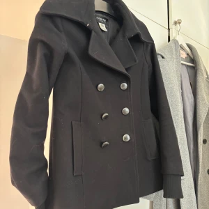 Svart kappa - Stilren svart kappa från Patrizia pepe. Jackan har långa ärmar, två fickor framtill och är tillverkad i ett mjukt ullmaterial. Perfekt för dig som gillar klassisk och tidlös stil. Storlek 40 egentligen men passar som S och XS.