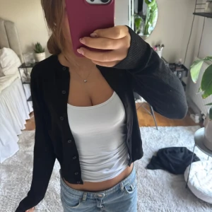 Svart kofta från H&M  - En svart, klassisk kofta från H&M med rund halsringning och knappar framtill. Långärmad och i mjuk bomullsblandning, perfekt att slänga över ett linne eller t-shirt.🥰🥰