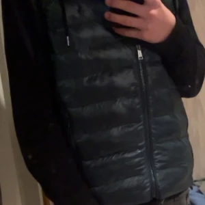 Mörkgrön väst Polo Ralph Lauren - Säljer en mörkgrön dunväst från Polo Ralph Lauren i storlek S med klassisk broderad logga på bröstet. Västen har quiltad design, dragkedja framtill och hög krage. Perfekt att slänga över en hoodie för en clean look. Mycket bra skick!