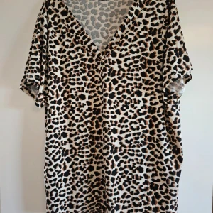 Leopardmönstrad t-shirt myWear Woman - Säljer en loose-fit t-shirt från myWear Woman med v-ringad hals och leopardmönster i beige, svart och bruna toner. Tröjan har korta ärmar och är tillverkad i ett mjukt syntetmaterial som känns skönt mot huden. Perfekt för dig som gillar djurprint och vill sticka ut.