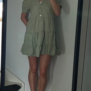 Grön kort klänning från Zara - Supersöt ljusgrön kort klänning från Zara med volangkjol och knappar framtill. Klänningen har korta puffärmar, krage och är tillverkad i linnematerial. .
