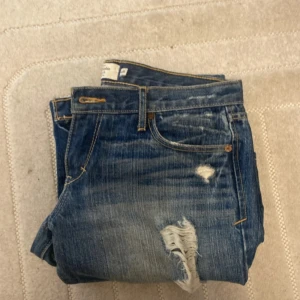 Blå bootcut jeans Abercrombie & Fitch - Snygga blå jeans från Abercrombie & Fitch i bootcut-modell med slitna detaljer och hål på benen. Storlek står ej men passar mig som har storlek 34 och är 166 lång. 