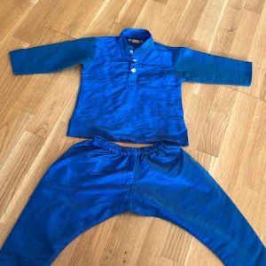 Blå sidenkostym med pärlknappar som man använder efter omskärelse  - Säljer en cool blå kostym för små barn i siden med långärmad överdel och matchande byxor. Överdelen har ståkrage och tre snygga pärlknappar framtill. Materialet har en glansig finish som ger en lyxig känsla. Perfekt för dig som gillar att sticka ut med färg och stil. Dena kostymen brukar man använda efter omskärelse det e därför den har en sån design på byxorna  