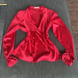 Festtopp❤️ - Snygg röd blus i glansig satin från More&More. Djup v-ringning med twistad detalj framtill, långa ärmar med manschett och en lätt figursydd passform. Perfekt att styla med jeans eller kjol för en trendig look. Passar mig fint som är xs/s