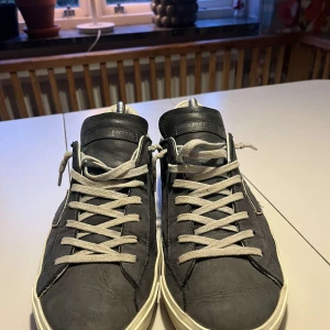 Philippe Model blå sneakers  - Snygga blå sneakers från Philippe Model med vita detaljer. Skorna har vit sula, ljusa skosnören och en ikonisk sköld på sidan. Bakpartiet är i ljust skinn med logga. Perfekta för dig som gillar stilrena och trendiga sneakers. Skorna är i använt skick men fortfarande stilrena och perfekta för dig som är ute efter nått trendigt!