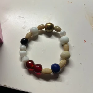 Färgglatt pärlarmband med stora pärlor - Unikt armband med stora pärlor i vitt, beige, rött, blått, svart och en guldig pärla. Pärlorna är runda och ovala och sitter på elastisk tråd. Perfekt accessoar för dig som gillar färg och personliga smycken.