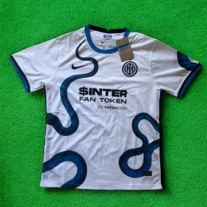 Inter Milan vit bortatröja Nike - Inter Milans officiella bortatröja från Nike i vitt med blå och svarta ormliknande detaljer. Tröjan har korta ärmar, blå krage och muddar samt tryckta loggor från Inter, Nike och sponsorer. Tillverkad i lätt och ventilerande Dri-FIT-material.