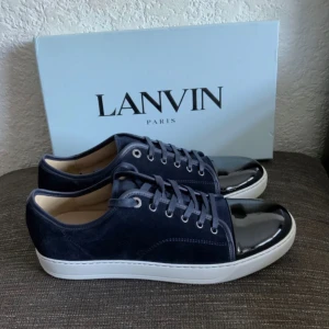 Mörkblå sneakers från Lanvin - Snygga mörkblå sneakers från Lanvin med ovandel i mocka och lackad tå. Skorna har vita platta sulor och klassisk snörning. Perfekta för dig som gillar stilrena och exklusiva detaljer.