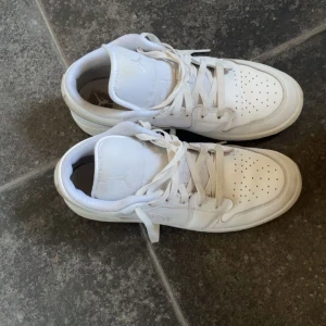 Nike Air Jordan 1 Low Triple White - Snygga Nike Air Jordan 1 Low i helvitt skinn med klassisk siluett och perforerad tå. Skorna har snörning, rund tå och ikoniska Air Jordan-loggan på hälen. Perfekta för dig som gillar stilrena sneakers med streetkänsla. Använt några gånger ungefär 6 gånger skorna är värda av 1500 när dem köptes