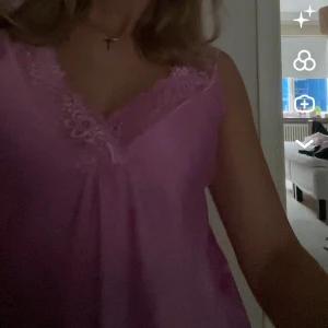 Rosa topp med spetsdetaljer - Söt rosa linnetopp med v-ringning och fina spetsdetaljer längs urringningen. Tunt och glansigt material som ger en mjuk känsla.  Nypris: 399 kr