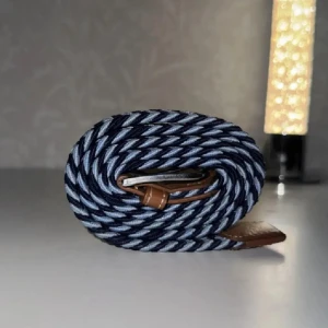 Randigt blått bälte med läderdetaljer - Snyggt randigt bälte i marinblått och ljusblått med bruna läderdetaljer vid spännet och änden. Bältet har en flätad design som ger en cool och modern look. Perfekt accessoar för att lyfta din outfit.