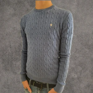 Blå kabelstickad 100% merinoull tröja Morris S - Snygg blå kabelstickad tröja från Morris i 100% merinoull. Tröjan har rund hals, lång ärm och en liten broderad logga på bröstet. Perfekt för dig som gillar klassisk stil med modern touch.