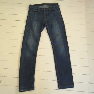 Lee Daren Button Fly jeans blå W30 L34 - Säljer ett par klassiska Lee Daren Button Fly jeans i mörkblå tvätt. Modellen har raka ben, fem fickor och snygga kontrastsömmar. Jeansen är tillverkade i slitstarkt bomullsmaterial och har Lee-logga på bakfickan och knappen framtill.