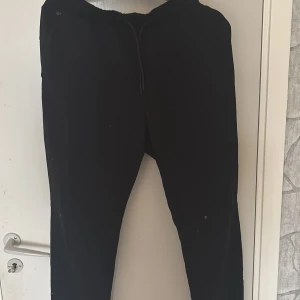 Svarta mjukisbyxor från SOC, stl L - Svarta mjukisbyxor från SOC i storlek L. Byxorna har elastisk midja med snörning och är tillverkade i mjukt material som passar perfekt för chill eller träning. Klassisk rak modell utan synliga loggor på benen.