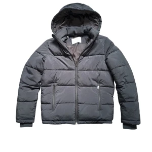 Selected Homme pufferjacka  - Den sitter som s/xs.  Svart pufferjacka från Selected Homme med huva och dragkedja framtill. Den har många fickor på insidan och så går det att göra den tajtare i midjan. Jackan har två sidofickor med dragkedja och quiltad design. Perfekt för kalla dagar när du vill hålla stilen enkel och clean.