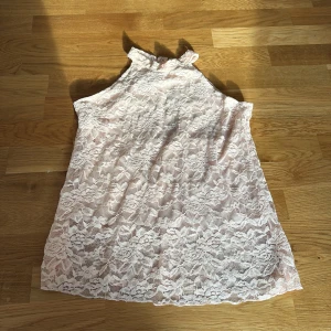 Ljusrosa tröja med öppen rygg - Säljer en superfin ljusrosa tröja i spets med hög hals och snygg öppning i ryggen. Tröjan är ärmlös och har ett romantiskt blommigt spetsmönster över hela. Perfekt för dig som gillar feminina detaljer och vill sticka ut med en söt look.