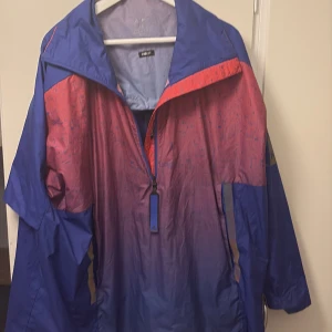 Adidas Parley blå/röd vindjacka M - Säljer en Adidas Parley vindjacka i blått och rött med coolt abstrakt mönster. Jackan har huva, halv dragkedja och är tillverkad i lätt polyester. Perfekt för dig som vill ha en sportig och snygg look. Står 'PACK IT' på insidan.