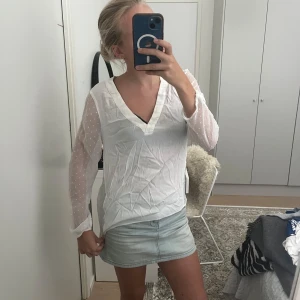 Vit blus med prickiga meshärmar - Säljer en vit blus med transparenta meshärmar som har små prickar. Ärmarna är långa och ger en söt och trendig känsla. Det finns en liten fläck på kragen.
