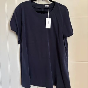 Mörkblå blus från Filippa K, storlek L  - Snygg mörkblå blus från Filippa K i storlek L. Modellen är rak och lite loose med korta ärmar och rund hals. Materialet är mjukt och har ett diskret randigt mönster. Perfekt för dig som gillar minimalistisk och stilren design.