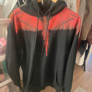 Marcelo Burlon svart hoodie med röd print - Svart hoodie från Marcelo Burlon County of Milan med ikoniskt rött vingmönster över axlar och bröst. Nästan helt ny, använd väldigt få gånger. Inga defekter. Pris går att diskutera.