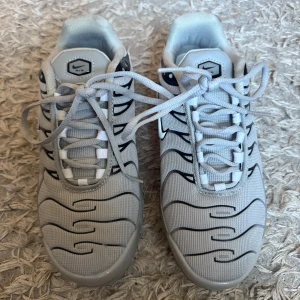 Nike Air Max sneakers i grått och svart - Nike Air Max sneakers i ljusgrå mesh med svarta vågformade detaljer och vit swoosh på sidan. Skorna har snörning och en synlig Air Max-sula för extra komfort. Perfekt för dig som gillar en sportig och modern look.