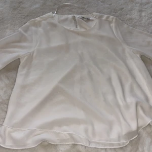 Vit blus från KappAhl, stl 36 - Säljer en stilren vit blus från KappAhl i storlek 36. Blusen har rund halsringning, trekvartsärmar och en snygg slitsdetalj baktill. Materialet är lätt och har en mjuk, lite glansig yta som ger en elegant känsla.