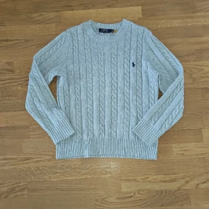 Ljusgrå kabelstickad tröja från Polo Ralph Lauren Stl S - Säljer en klassisk ljusgrå kabelstickad tröja från Polo Ralph Lauren med rund halsringning och broderad marinblå logga på bröstet. Perfekt för en stilren och tidlös look. Ulltröja från ralph lauren nypris ca 2500kr mitt pris 799kr. Priset är inte hugget i sten.