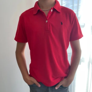 Röd Polo t-shirt med krage - Snygg röd t-shirt från Polo med klassisk krage och två knappar framtill. T-shirten har korta ärmar och är tillverkad i 100% bomull. Ej äkta 