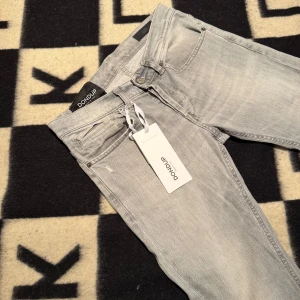 Ljusgrå jeans från Dondup - Snygga ljusgrå jeans från Dondup med klassisk femficksdesign och raka ben. Jeansen har diskreta slitningar och är tillverkade i mjuk bomullsdenim. Perfekta för dig som gillar en clean och stilren look. Storlek 29