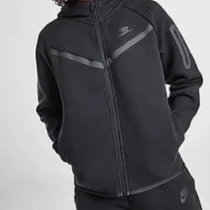 Svart hoodie från Nike med dragkedja - Svart hoodie från Nike med hel dragkedja framtill och diskreta grå detaljer över bröstet och på ena ärmen. Tröjan har huva och långa ärmar, perfekt för en sportig och avslappnad stil.
