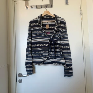 Randig kofta från Odd Molly med knyt - Säljer en stickad kofta från Odd Molly med blå, grå och beige ränder. Koftan har lång ärm, omlottmodell med knytband framtill och broderad Odd Molly-logga i rosa på ryggen. Perfekt för dig som gillar mönstrade och mysiga plagg med coola detaljer. Storlek 2 som enligt deras storleksguide motsvarar en storlek M. Fint skick, men den är mer använd och kan ha tecken på användning. 