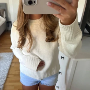 Vit stickad tröja med ribbade muddar - Säljer en vit stickad tröja med rund hals och ribbade muddar vid ärmslut och nederkant. Tröjan har en clean och enkel design, perfekt att matcha med jeans eller shorts. Långärmad och mjuk, passar dig som gillar en chill och stilren look.