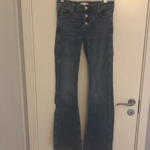 Blå bootcut jeans från Gina Tricot - Snygga blå jeans från Gina Tricot i bootcut-modell. Jeansen har klassisk femficksdesign, synliga silverfärgade knappar och är tillverkade i ett mjukt denimtyg.