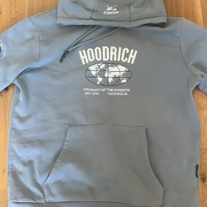 Grå hoodie från Hoodrich med tryck - Säljer en grå hoodie från Hoodrich i storlek M. Originalet kostar cirka 1200kr. Tröjan har vit och blå världskarta-tryck framtill, text på ärmen och klassisk känguruficka. Huva med snörning och mjukt material, perfekt för chill dagar. 