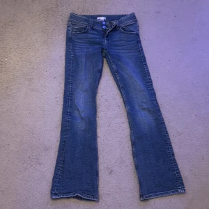 Blå bootcut jeans  - Snygga blå jeans från Gina Tricot i modell med bootcut. Klassisk femficksdesign, dubbla knappar i midjan och lätt slitna detaljer. Perfekta för dig som gillar en tidlös och avslappnad look.