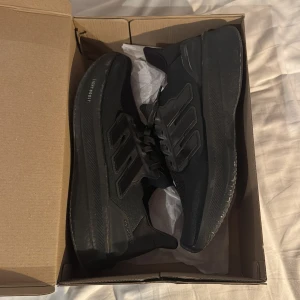 Adidas Ultraboost 5  - Säljer ett par helsvarta Adidas Ultraboost 5 sneakers med klassiska tre ränder på sidan. Skorna har en chunky sula med boost-dämpning och ovandel i syntet och mesh. Perfekta för dig som gillar sportig och clean stil. Snygga och bekväma för både träning och vardag.