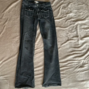 Mörkgrå bootcut jeans med fickdetaljer - Snygga mörkgrå jeans från Gina tricot med bootcut-ben och coola fickor framtill med lock och knapp. Jeansen har låg midja och är gjorda i klassiskt denim med tydliga sömmar. Perfekta för dig som gillar en avslappnad men trendig stil.