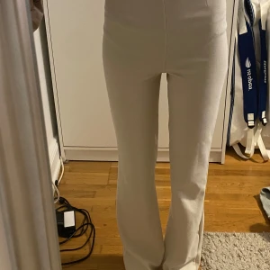 Vita raka byxor med hög midja - Säljer ett par stilrena vita byxor med hög midja och raka ben. Byxorna har en clean look utan synliga fickor eller detaljer och är perfekta för en fräsch och modern stil. Materialet känns mjukt och stretchigt, vilket gör dem riktigt bekväma.